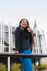 Von unten Seitenansicht einer asiatischen Unternehmerin in schickem lässigen Stil, die in der Innenstadt auf der Straße steht und mit dem Handy telefoniert, während sie wegschaut — Stockfoto