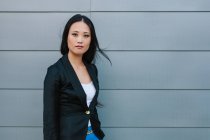 Femme entrepreneure asiatique confiante debout dans la rue près du bâtiment urbain et regardant la caméra — Photo de stock