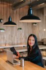 Zufriedene Unternehmerin sitzt mit Tablet und Laptop am Tisch, während sie an einem Projekt arbeitet und wegschaut — Stockfoto