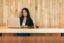 Umtriebige asiatische Unternehmerin sitzt im Café am Tisch, isst Sushi und arbeitet per Netbook an einem Remote-Projekt — Stockfoto