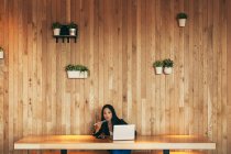 Femme entrepreneure asiatique occupée assise à table dans un café tout en mangeant des sushis et en travaillant sur un projet à distance via netbook — Photo de stock