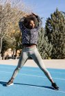 Жирна афроамериканська спортсменка, що стоїть на стадіоні і розтягує тіло під час нагрівання з піднятими руками перед тренуванням в сонячний день і озирається. — стокове фото