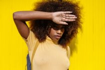 Young ethnic female with Afro hairstyle standing on yellow wall and looking at camera — Stock Photo