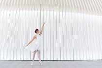 Молодая балетная танцовщица на цыпочках в пуантах с поднятыми ногами и руками танцует на тротуаре на открытом воздухе — стоковое фото