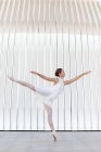 Вид збоку молодої балетної танцівниці в туфлях з піднятою ногою і рукою танцює на плитковому тротуарі на відкритому повітрі — стокове фото