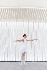 Junge Balletttänzerin in Zehenspitzen in Spitzenschuhen mit erhobenem Bein und erhobenem Arm tanzt auf gefliestem Bürgersteig im Freien — Stockfoto
