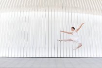 Молода танцівниця балету в взутті з піднятою ногою і рукою стрибає через плитковий тротуар — стокове фото