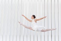 Молодая балетная танцовщица в пуантах с поднятой ногой и рукой, прыгающая через мостовую — стоковое фото