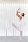 Seitenansicht einer jungen Balletttänzerin in Zehenspitzen in Spitzenschuhen mit erhobenem Bein und erhobenem Arm, die auf gefliestem Bürgersteig im Freien tanzt — Stockfoto