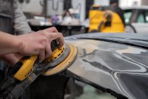 Анонимный мужчина-механик, использующий машину для полировки автомобиля при подготовке автомобиля к покраске в мастерской — стоковое фото