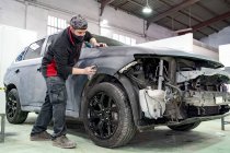 Baixo ângulo do mestre masculino em trabalho sujo buffing automóvel enquanto prepara o veículo para pintura em serviço de reparação — Fotografia de Stock