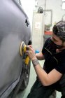 Vue latérale mécanicien masculin utilisant la machine pour polir la voiture tout en préparant l'automobile pour la peinture en atelier — Photo de stock