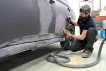 Боковой вид мужской механик с помощью машины для полировки автомобиля при подготовке автомобиля к покраске в мастерской — стоковое фото