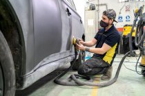 Seitenansicht männlicher Mechaniker mit einer Maschine zum Polieren des Autos, während er das Auto für die Lackierung in der Werkstatt vorbereitet — Stockfoto