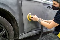 Боковой вид мужской механик с помощью машины для полировки автомобиля при подготовке автомобиля к покраске в мастерской — стоковое фото