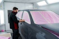 Mecánico masculino ocupado en cinta adhesiva máscara en el coche antes de pintar en el taller - foto de stock