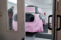 Ocupado mecânico masculino em fita adesiva máscara no carro antes de pintar na oficina — Fotografia de Stock