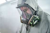 Mechaniker zieht Atemschutzmaske und Schutzanzug an, während er sich in der Werkstatt auf die Autolackierung vorbereitet — Stockfoto