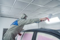 Side view of male in respiratory mask and protective suit painting car with spray gun in service — Stock Photo