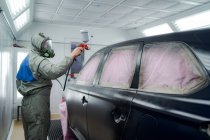 Вид сбоку на мужчину в респираторной маске и автомобиль с краской защитного костюма с автоматом в эксплуатации — стоковое фото