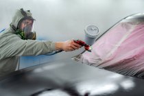 Seitenansicht des Mannes in Atemschutzmaske und Schutzanzug Malerei Auto mit Spritzpistole im Einsatz — Stockfoto