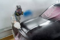 From above male in respiratory mask and protective suit painting car with spray gun in service — Stock Photo