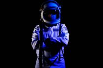 Hombre cosmonauta con traje espacial blanco y casco mientras está de pie sobre fondo negro en luz de neón azul - foto de stock