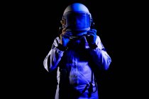 Male cosmonaut wearing white space suit and helmet while standing on black background in blue neon light — Stock Photo