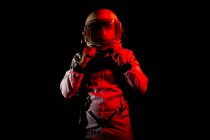 Male cosmonaut wearing white space suit and helmet while standing on black background in red neon light — Fotografia de Stock
