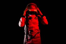 Male cosmonaut wearing white space suit and helmet while standing on black background in red neon light — Fotografia de Stock