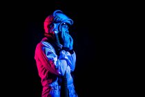 Side view of male cosmonaut wearing white space suit and helmet while standing on black background in pink and blue neon light looking away — Fotografia de Stock
