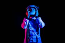 Male cosmonaut wearing white space suit and helmet while standing on black background in pink and blue neon light looking away — Stock Photo