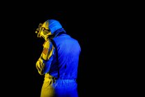 Back view of unrecognizable male cosmonaut wearing white space suit and helmet while standing on black background in blue and yellow neon light — Fotografia de Stock
