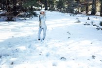 Astronauta joven enfocada en traje espacial y casco mirando hacia otro lado y de pie en un bosque nevado - foto de stock