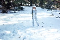Focused young female astronaut in spacesuit and helmet looking away and standing in snowy woodland — Stock Photo