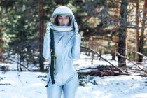 Konzentrierte junge Astronautin in Raumanzug und Helm blickt in die Kamera und steht im verschneiten Wald — Stockfoto