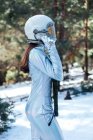 Вид сбоку на сфокусированную неузнаваемую молодую астронавтку в скафандре и шлеме, стоящую в заснеженной лесистой местности — стоковое фото
