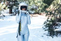 Focused unrecognizable young female astronaut in spacesuit and helmet standing in snowy woodland — Stock Photo