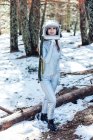 Сосредоточенная молодая женщина-астронавт в скафандре и шлеме смотрит в сторону и стоит в заснеженной лесистой местности — стоковое фото