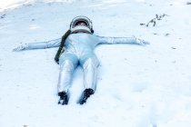 Full body fit calm spacewoman in costume and helmet lying with arms outstretched on snowy glade in winter forest — Fotografia de Stock