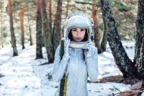 Konzentrierte junge Astronautin in Raumanzug und Helm blickt in die Kamera und steht im verschneiten Wald — Stockfoto