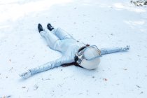 Full body fit calm spacewoman in costume and helmet lying with arms outstretched on snowy glade in winter forest — Stock Photo
