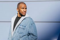 Unemotional cool African American male in casual wear with hands in pockets looking up in city looking away — Photo de stock