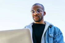 Da sotto etnico afroamericano adulto maschio dipendente remoto con computer portatile seduto in città — Foto stock