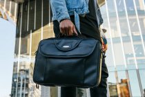 From below cropped unrecognizable adult ethnic male in casual outfit with leather briefcase strolling in town — Stock Photo