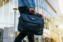 From below cropped unrecognizable adult ethnic male in casual outfit with leather briefcase strolling in town — Stock Photo