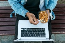 From above crop dreamy ethnic male distance worker with delicious lunch in container sitting with netbook in city and looking away — Stock Photo