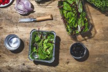 Vista dall'alto disposizione di foglie fresche mix insalate in ciotole da asporto posto sul tavolo vicino olive nere e cipolle tagliate — Foto stock