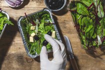 Top view crop anonymous chef in glove adding black olives to mix leaves salad with butter cubes — Photo de stock
