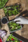 Top view coltivare anonimo chef in guanto aggiungendo olive nere e foglie per mescolare insalata foglie con cubetti di burro — Foto stock